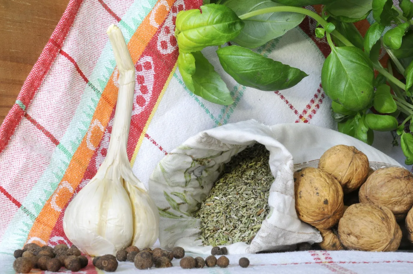 Usturoi proaspăt și nuci lângă un săculeț de pânză cu plante uscate, pe un prosop de bucătărie